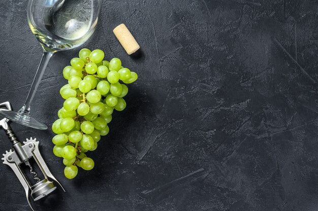 Una rama de uvas verdes, una copa de vino, un sacacorchos y un corcho. Concepto de vinificación.