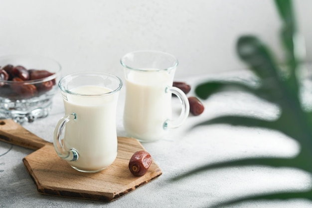 Ramadán Kareem alimentos y bebidas Plato de dátiles vaso de leche y rama de palmera datilera sobre fondo gris claro Estilo de vida musulmán justo Lugar para el texto Enfoque selectivo