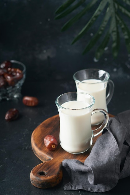 Ramadán Kareem alimentos y bebidas Plato de dátiles vaso de leche y rama de palmera datilera sobre fondo negro Justo estilo de vida musulmán Comida vegetariana Enfoque selectivo