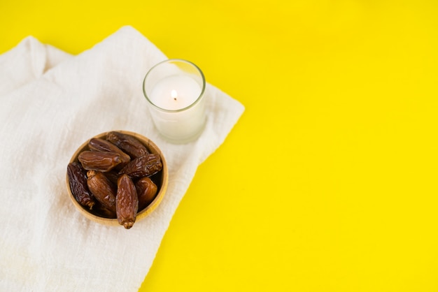 Foto ramadan kareem festival. feche acima das datas secadas frutificam na bacia com vela no fundo amarelo. copie o espaço.