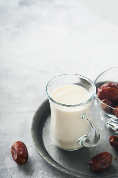 Ramadan Kareem Speisen und Getränke Teller mit Datteln Glas Milch und Dattelpalmenzweig auf hellgrauem Hintergrund Gerechter muslimischer Lebensstil Platz für Text Selektiver Fokus