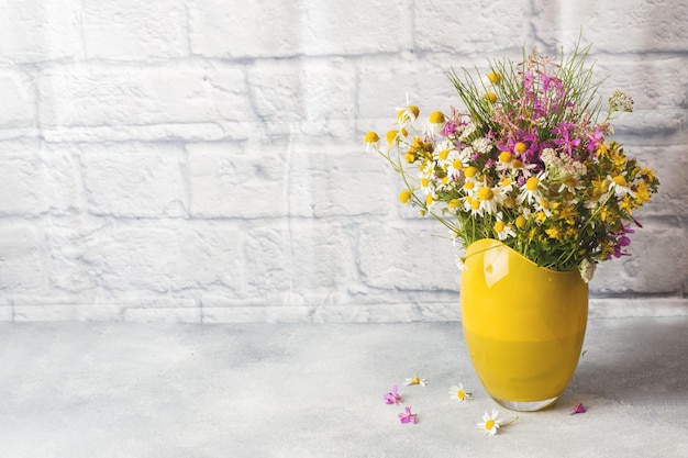 Ramalhete de wildflowers bonitos no vaso em uma superfície cinzenta com espaço da cópia.