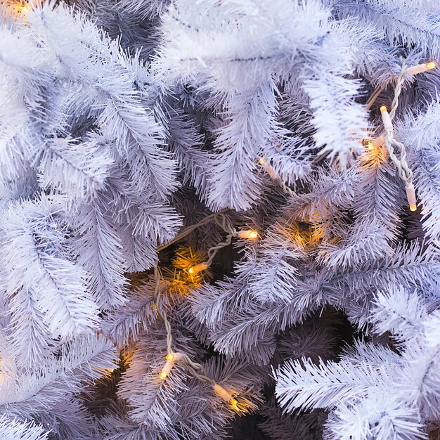 Ramas de abeto blanco de un árbol de Navidad artificial con luces amarillas. Fondo y copia espacio.