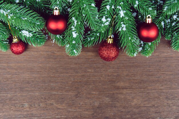 Ramas de abeto, bola de Navidad roja y piñas con decoración de nieve en una tabla de madera