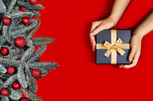 Ramas de abeto con bolas rojas de Navidad y manos de mujer con un regalo