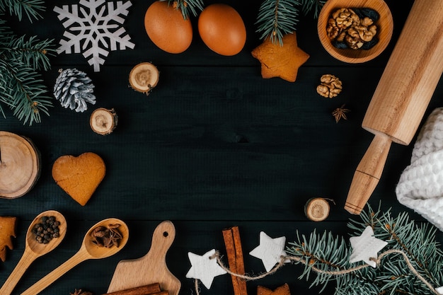 Ramas de árbol de Navidad, galletas de jengibre, accesorios para hornear e ingredientes en la mesa de madera negra. Copia espacio