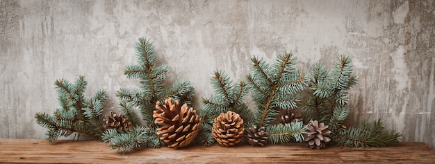 Ramas de los árboles de Navidad con conos en una tabla de madera contra un muro de hormigón gris.