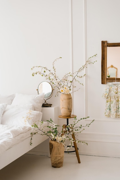 Ramas de árboles primaverales con flores blancas en jarrones en el interior de un dormitorio blanco de estilo escandinavo