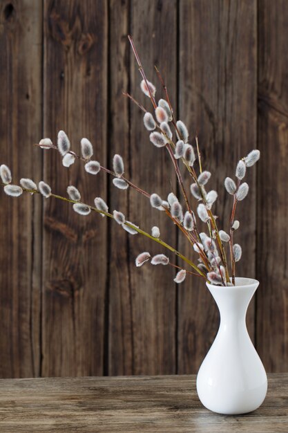 Ramas de flores de sauce en florero sobre fondo de madera