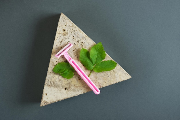 Ramas y hojas de menta y navaja de afeitar femenina rosa de plástico desechable sobre piedra triangular, fondo verde oscuro