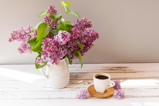 Ramas de lilas frescas en una jarra sobre una mesa de madera blanca, una taza de café. el concepto de vida en el campo.