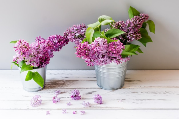 Ramas de lilas púrpuras de primavera en cubos sobre una mesa de madera blanca.