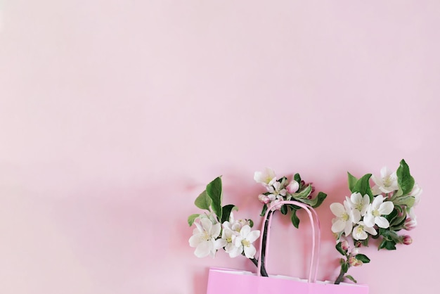 Las ramas de un manzano con flores se encuentran en una bolsa de papel sobre un fondo de color rosa