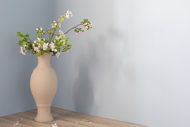 Ramas de manzano con flores en jarrón de piso contra la pared gris