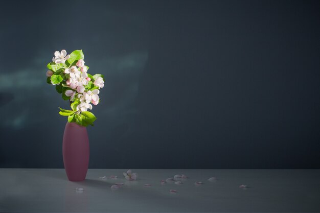 Ramas de manzano con flores en jarrón rosa en la superficie de la pared azul