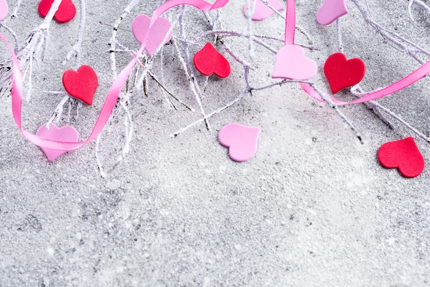 Ramas en la nieve con corazones rosados y rojos en un fondo concreto