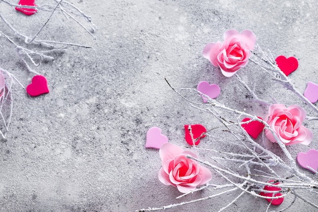 Ramas en la nieve con rosa rosa brotes y corazones sobre un fondo concreto