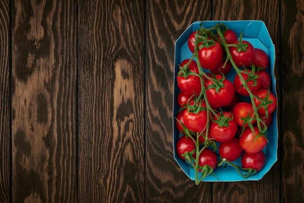 Ramas de tomate cherry en bandeja de embalaje de cartón sobre fondo de madera