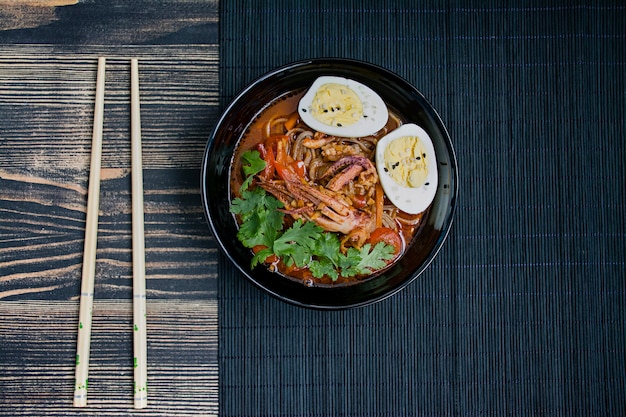 Ramen japonês com frutos do mar, ervas e ovos em conserva em uma superfície escura