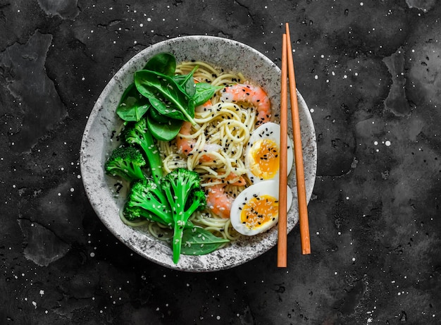 Ramen-Nudeln mit Garnelen-Brokkoli-Spinat und gekochtem Ei auf dunklem Hintergrund Draufsicht Köstliches Mittagessen im asiatischen Stil