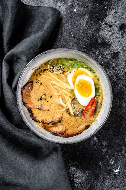 Ramen de sopa japonesa tradicional con caldo de carne, fideos asiáticos, algas, carne de cerdo en rodajas, huevos. Fondo negro. Vista superior