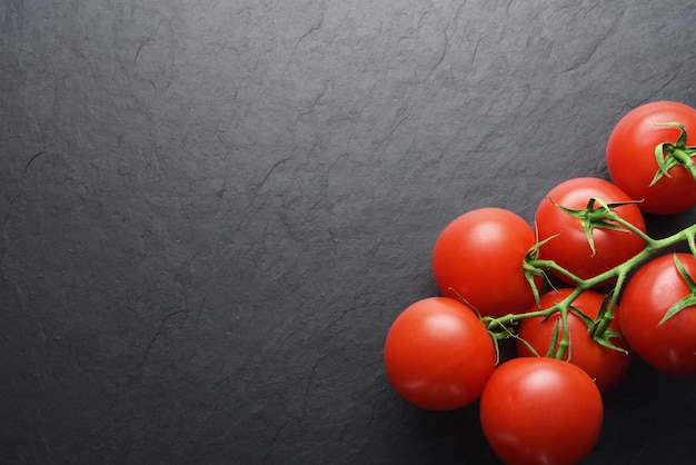 Ramifique com tomates vermelhos maduros em ardósia preta com espaço de cópia