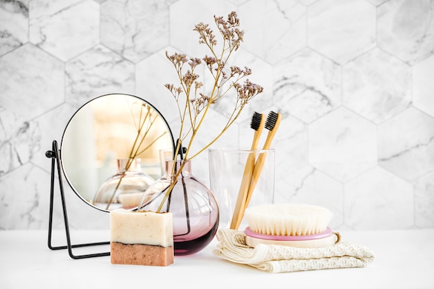 Ramifique em um vaso de vidro, espelho, escova de dentes de bambu e produtos cosméticos na mesa branca. Decoração para interiores. Decoração elegante para casa.