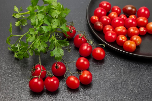 Raminho de salsa e raminho de tomate cereja vermelho na mesa Pequenos tomates vermelhos na chapa preta