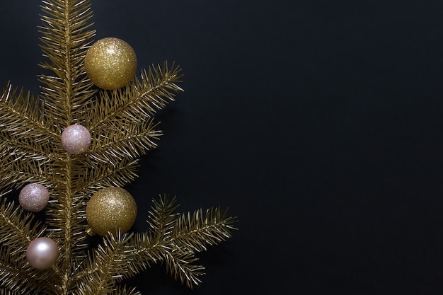 Ramita de Navidad dorada con pequeñas bolas de oro y rosa sobre superficie negra