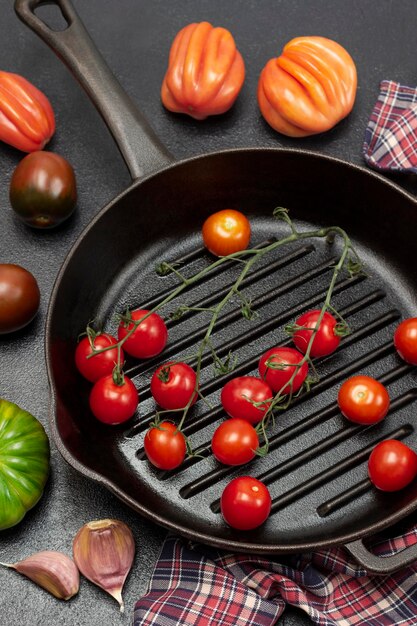 Una ramita de tomate cherry en una sartén Tomates y dientes de ajo en la mesa