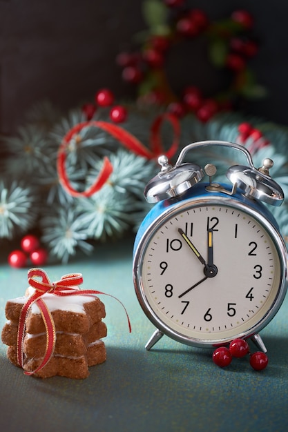 Foto ramitas de abeto navideño, bayas rojas, galletas estrelladas y reloj despertador azul vintage de cinco a doce.