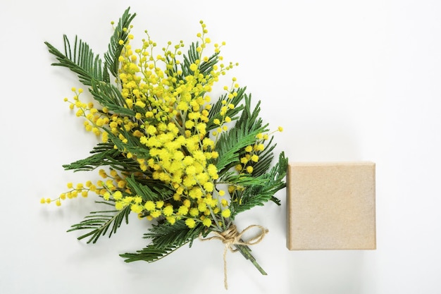 Un ramo amarillo de mimosa y una caja de regalo y una bolsa de papel kraft Tarjeta de felicitación para el Festival de Primavera del Día Internacional de la Mujer 8 de marzo Espacio de copia de Pascua