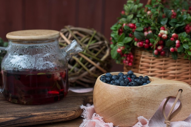 Un ramo de bayas de lingonberry rojas maduras en una canasta de mimbre y una tetera de té de lingonberries setas de chanterelle de naranja del bosque