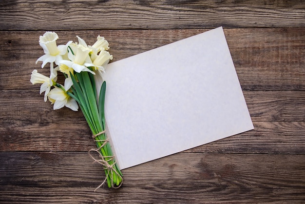 Ramo de blanco con narcisos amarillos y hoja de papel para escribir sobre fondo de madera