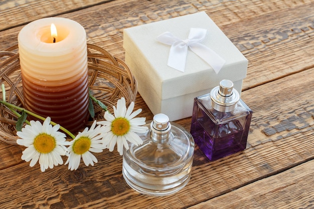 Ramo de chamomiles perfumes vela encendida y caja de regalo blanca sobre tablas de madera Vista superior