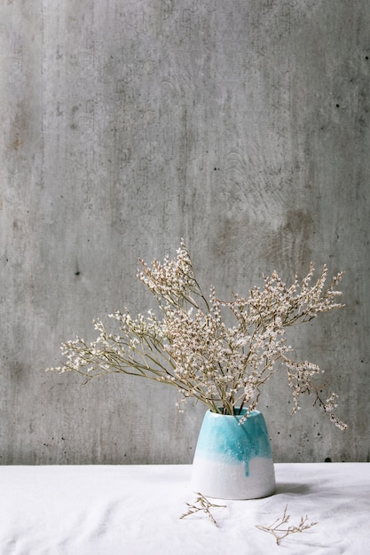 Ramo de flores brancas secas em vaso de cerâmica branca em toalha de mesa de linho branca com parede cinza atrás