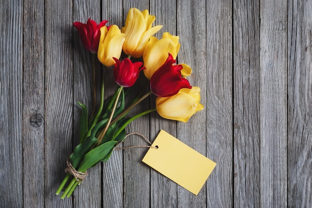 Ramo de flores de tulipa com cartão de nome em branco em fundo de madeira, espaço de cópia