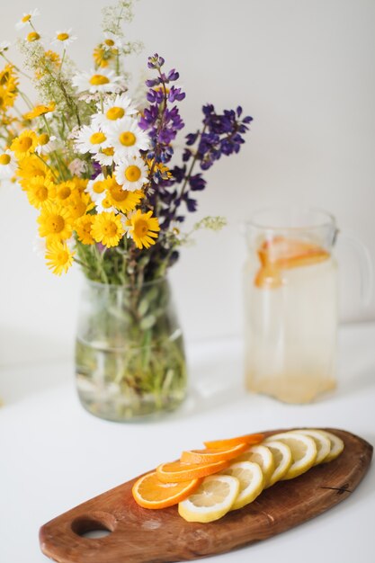Ramo de flores silvestres naturais em um vaso e limonada caseira com laranjas e limões