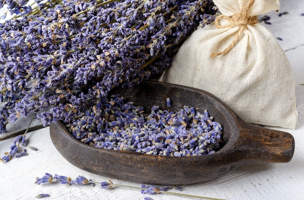 Ramo de lavanda seca, flores de lavanda em uma tigela de madeira e bolsa sachê de têxteis em uma mesa de madeira rústica branca closeup.