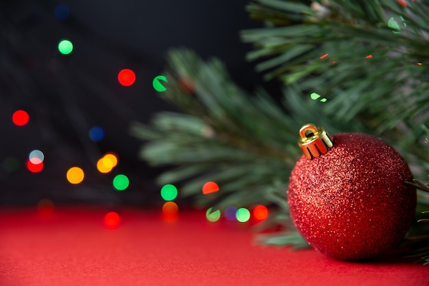 Ramo de pinho verde e close-up da bola de Natal brilhante vermelho sobre um fundo vermelho e preto. Feriado tradicional de inverno. Lindo ano novo ou fundo de Natal, cartão postal. Bokeh, foco seletivo, copie o espaço.