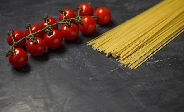 Ramo de tomate cereja e ingredientes crus de espaguete para fazer massas italianas em foco seletivo de fundo escuro