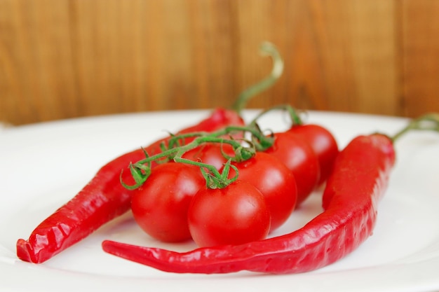 ramo de tomates de cereja vermelha e duas vagens de pimentas no prato branco