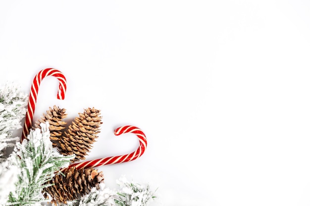 Ramo decorativo spruce coberto de neve com cones e doces de natal em uma parede branca. espaço para texto.