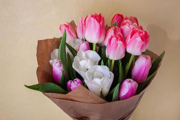 Ramo de delicados tulipanes rosados y blancos en papel artesanal sobre un fondo claro