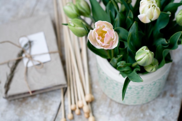 Ramo de delicados tulipanes rosas y agujas para tejer sobre un fondo de madera