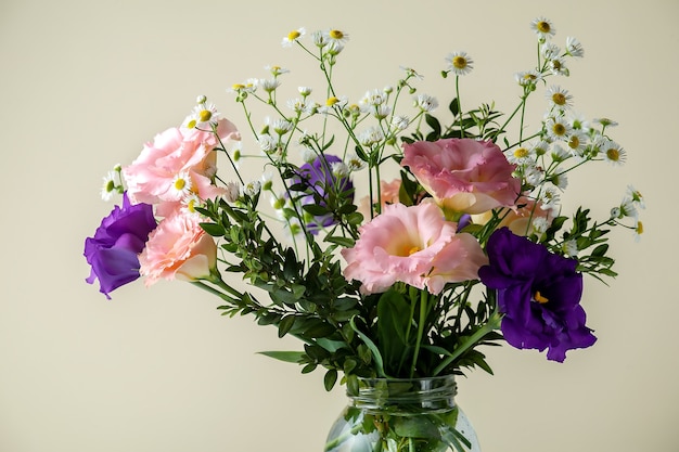 Ramo de eustoma con boj y ramas de hoja pequeña sobre una mesa sobre un fondo amarillo