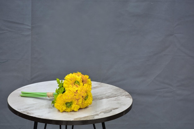 ramo de flores amarillas en una mesa redonda de madera con fondo gris