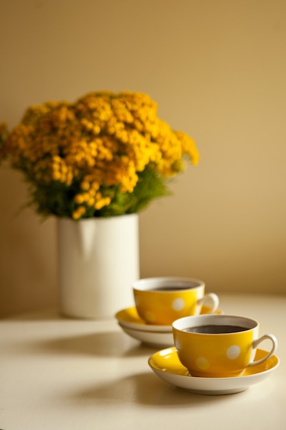 Ramo de flores amarillas sobre la mesa - Dos tazas de café amarillas sobre fondo blanco, coffee break y concepto de adicción a la cafeína. diseño vintage y estilo retro