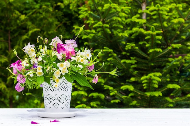 Ramo de flores de aquilegia, jazmín y trébol en un jarrón blanco sobre una mesa blanca