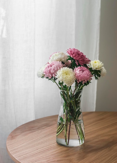 Ramo de flores de aster otoñal en un jarrón de cristal sobre una mesa redonda de madera